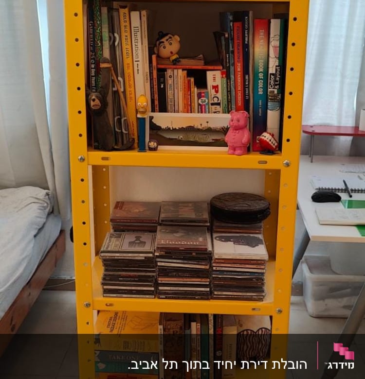 מדף צהוב עם ספרים ודיסקים מסודרים